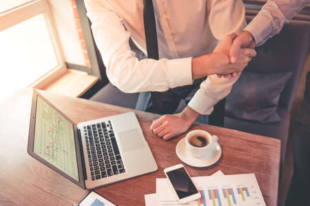 Cropped image of handsome business partners shaking hands while meeting in cafeの写真素材