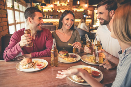 Happy friends are eating, drinking, talking and smiling while spending time together in cafe