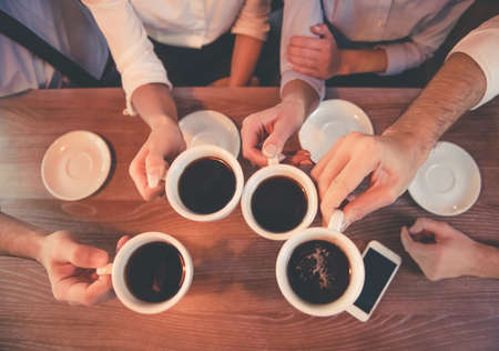 Top view of business people holding cups of coffee while having coffee break in cafeの写真素材