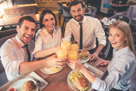 Business people are clinking glasses and smiling while spending time together in cafe