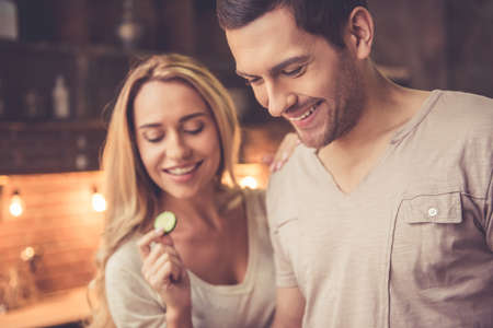 Beautiful young couple is smiling while cooking together in kitchen at homeの写真素材