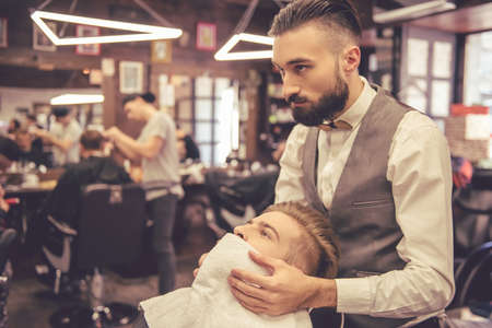 Handsome bearded man is getting beard hairstyle by hairdresser at the barbershopの写真素材