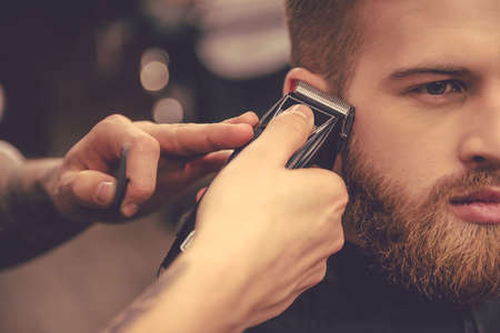 Cropped image of handsome bearded man getting haircut by hairdresser at the barbershopの写真素材