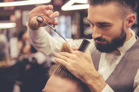 Attractive hairdresser is cutting his handsome client's hair at the barbershopの写真素材
