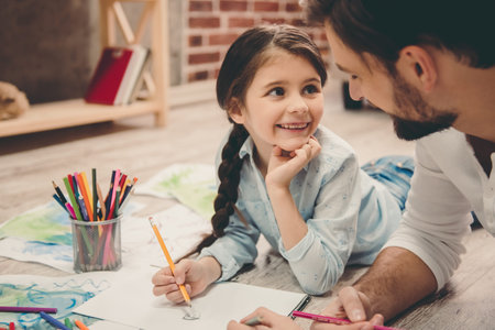 Cute little girl and her handsome father are drawing and smiling while playing together at homeの写真素材