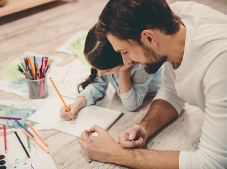 Cute little girl and her handsome father are drawing and smiling while playing together at homeの写真素材