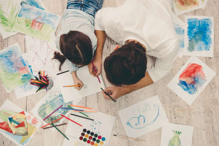Top view of little girl and her father drawing while playing together at homeの写真素材