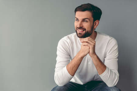 Handsome young man is looking away and smiling, on gray backgroundの写真素材