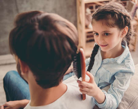 Cute little girl is combing her handsome father and smiling while they are playing together at homeの写真素材