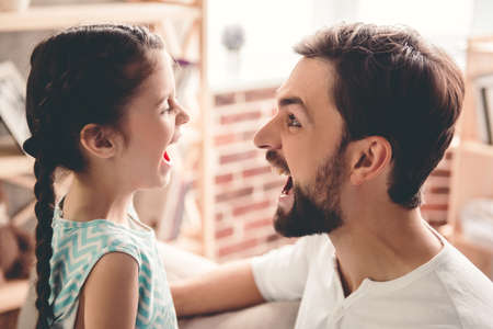 Cute little girl and her handsome father are playing together at homeの写真素材