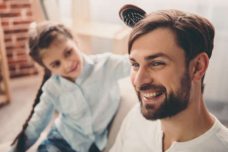 Cute little girl is combing her handsome father and smiling while they are playing together at homeの写真素材