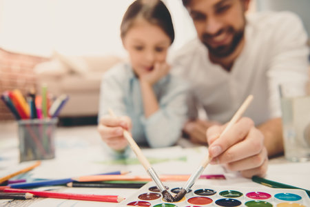 Cute little girl and her handsome father are drawing and smiling while playing together at homeの写真素材