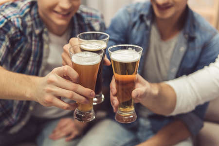 Cropped image of attractive guys clinking glasses of beer and smiling while resting at homeの写真素材