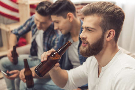 Attractive guys are drinking beer, talking and smiling while resting at homeの写真素材