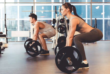 Attractive young people are working out with barbell in gymの写真素材