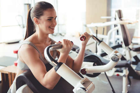 Beautiful young woman is smiling while working out in gymの写真素材