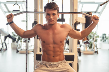 Attractive young muscular man is working out on a fitness station in gym, pumping iron