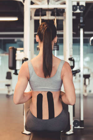 Back view of beautiful young woman working out on a fitness station, pumping iron in gymの写真素材