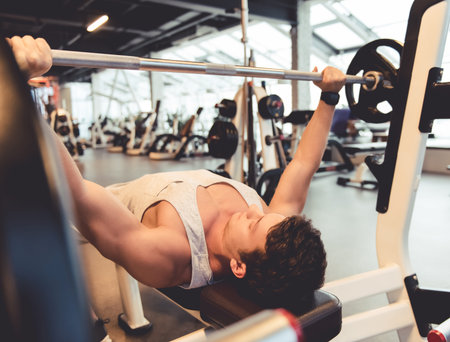 Attractive young muscular man is lifting weight while working out in gym