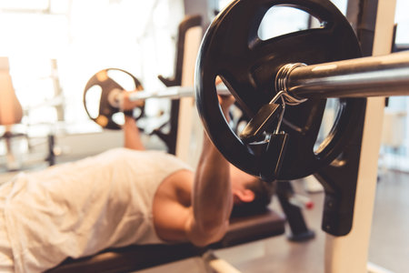 Attractive young muscular man is lifting weight while working out in gymの写真素材