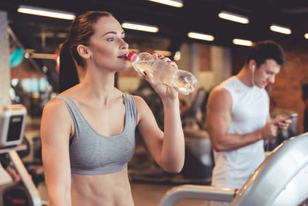 Attractive young woman is drinking water while running on a treadmill in gymの写真素材