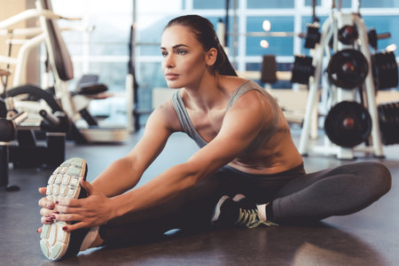 Attractive young woman is smiling while stretching body in gymの写真素材