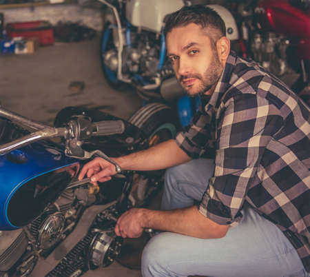 Handsome confident man is looking at camera while repairing a motorcycle in the repair shopの写真素材
