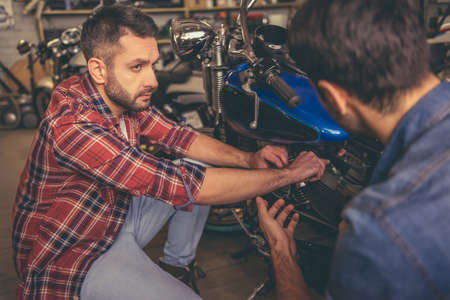 Handsome guys are talking while repairing a motorcycle in the repair shopの写真素材