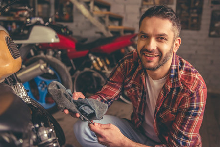 Handsome man is looking at camera and smiling while repairing a motorcycle in the repair shop