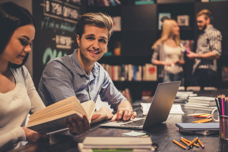 Young smart people are using gadgets and books and smiling while working hard in the modern library