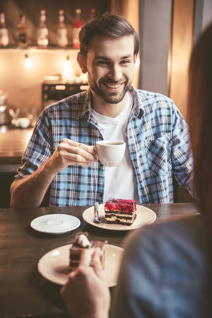 Happy young couple is holding hands, drinking coffee and smiling while sitting at the cafeの写真素材