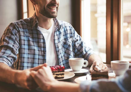 Cropped image of happy young couple holding hands and smiling while sitting at the cafeの写真素材