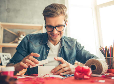 Handsome romantic guy is smiling while making present for his coupleの写真素材