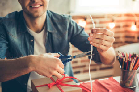 Cropped image of handsome romantic guy smiling while making present for his coupleの写真素材