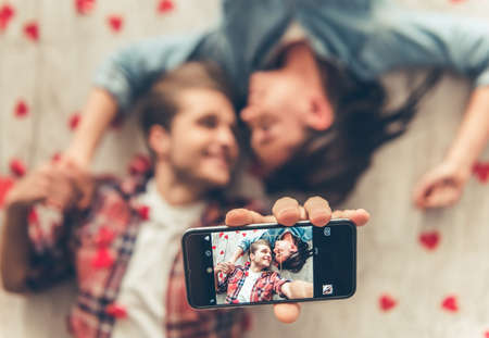 Top view of happy young couple doing selfie using a smart phine and smiling while lying on wooden floorの写真素材