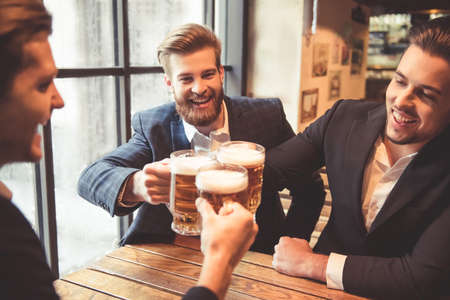 Handsome businessmen are clinking glasses of beer and smiling while resting at the pubの写真素材
