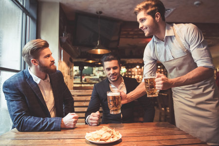 Handsome businessmen are drinking beer, talking and smiling while resting at the pub