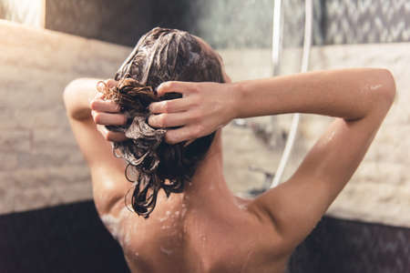 Back view of beautiful naked young woman washing her hair while taking shower in bathroomの写真素材