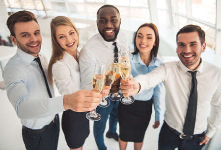 Successful business people are clinking glasses of champagne and smiling while celebrating in officeの写真素材