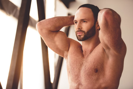 Portrait of handsome muscular man with bare torso looking forward while standing in gym