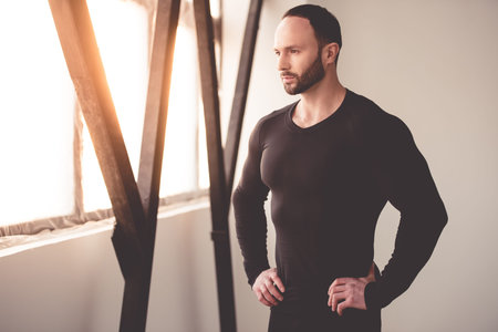 Portrait of handsome muscular man in black close-fitting jumper looking out the window