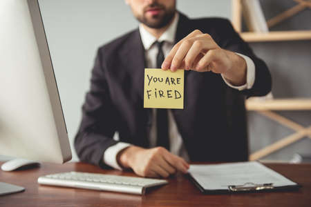 Cropped image of boss holding a note "you are fired" while sitting at the table in his officeの写真素材