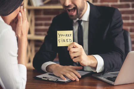 Cropped image of angry boss firing young business woman and yelling while sitting in his officeの写真素材
