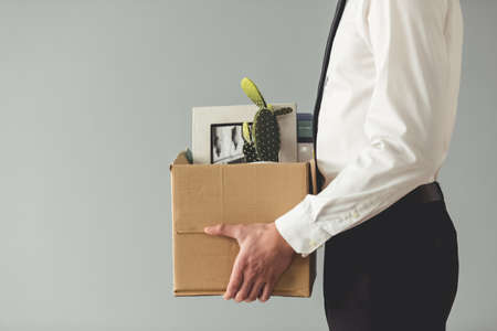 Getting fired. Cropped image of handsome businessman in formal wear holding a box with his stuff, on gray backgroundの写真素材