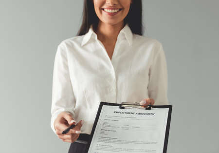 Cropped image of beautiful young business woman offering to sign an employment agreement and smiling, on gray backgroundの写真素材