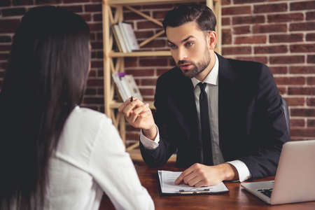 Handsome employer in suit is conducting a job interview while sitting in his officeの写真素材
