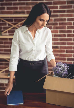 Getting fired. Beautiful young business woman in formal wear is packing her stuff into the boxの写真素材