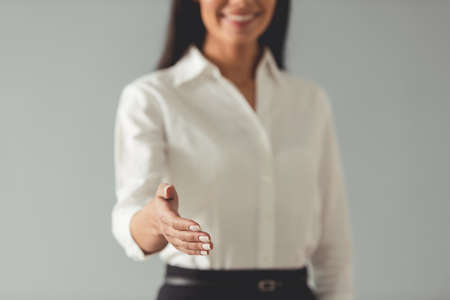 Cropped image of beautiful young business woman offering her hand and smiling, on gray backgroundの写真素材