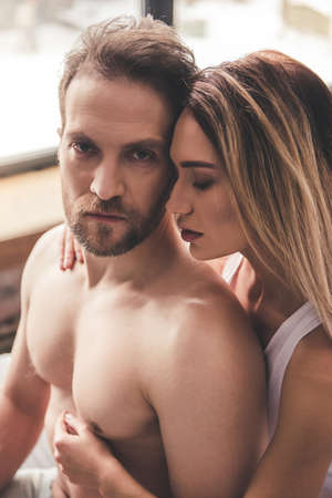 Beautiful couple is hugging while spending time together in bed at homeの写真素材