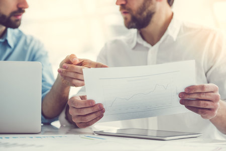 Two handsome businessmen are examining and discussing documents while working in officeの写真素材